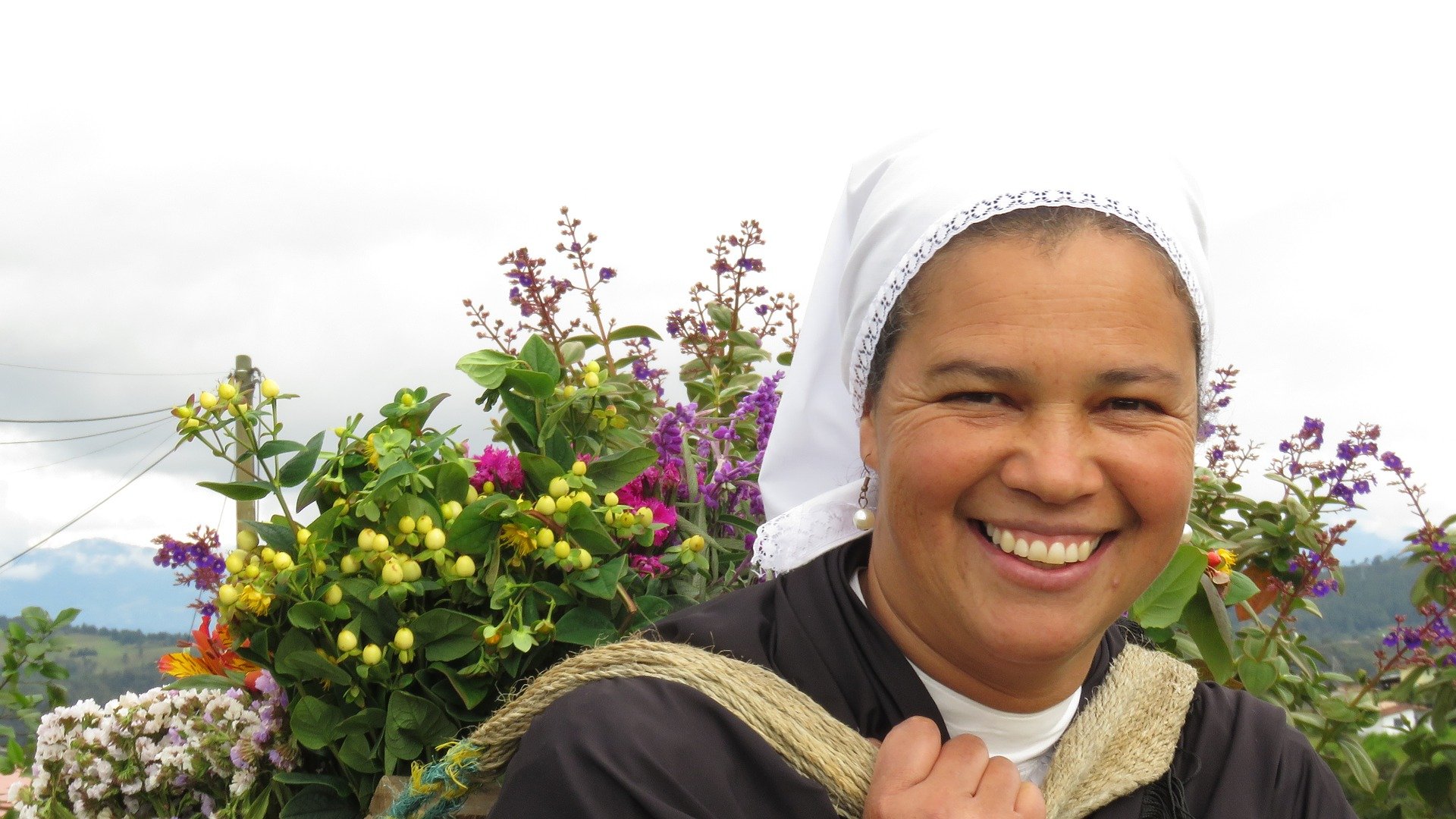 Mujer silletera sonriente cargando silleta de flores en la espalda