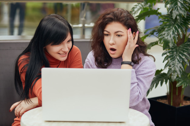 Dos mujeres mirando información en un  computador. Una mujer con rostro sonriente, la otra mujer con rostro de asombro.